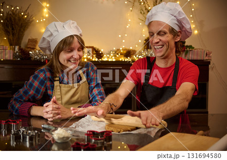 Joyful Holiday Baking With Friends: Two People in Chef Hats Rolling Dough and Laughing in a Cozy Festive Kitchen Joyful Holiday Baking With Friends: Two People in Chef Hats Rolling Dough and Laughing in a Cozy Festive Kitchen 131694580