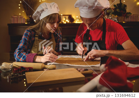 Cooking Duo in Chef Hats Rolling Dough Together for Christmas Treats in a Cozy Kitchen 131694612