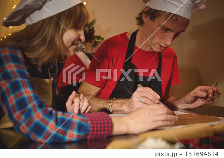 Two Chefs Crafting Holiday Treats in a Warm Kitchen With Dough, Cookie Cutter, and Festive Lights 131694614