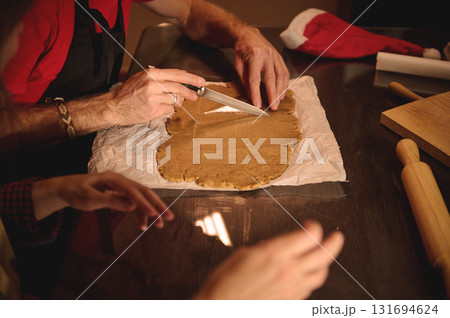 Family Christmas Baking Session: Hands Cutting Dough on Parchment with Santa Hat and Rolling Pin Family Christmas Baking Session: Hands Cutting Dough on Parchment with Santa Hat and Rolling Pin 131694624