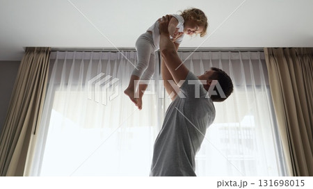 Father tossing daughter shares playful moment against window Father tossing daughter shares playful moment against window 131698015