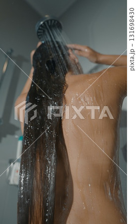A woman enjoys a delightful shower with her long hair flowing beautifully under soothing water 131698430