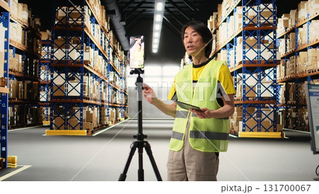 Asian worker promoting the large business industrial warehouse in a vlog, live streaming a video for e-commerce shipment advertisement. Staff presenting the storage on commercial ad. Camera A. Asian worker promoting the large business industrial warehouse in a vlog, live streaming a video for e-commerce shipment advertisement. Staff presenting the storage on commercial ad. Camera A. 131700067