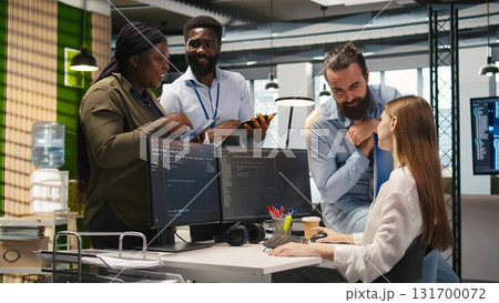 Startup newcomer making friends in office, learning how to use machine learning tech. Upbeat young girl in workplace chatting with coworkers while using AI predictive models, camera A 131700072