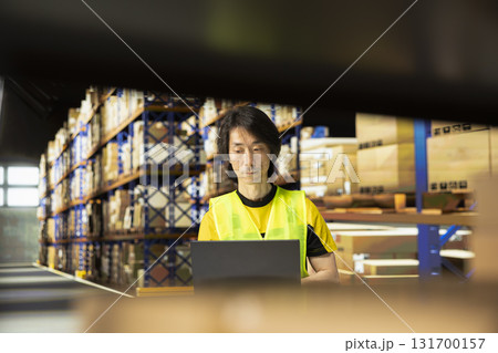 Warehouse employee in workwear preparing packages for local delivery, processing custom orders and handling merchandise within large business operation focused on e-commerce. Warehouse employee in workwear preparing packages for local delivery, processing custom orders and handling merchandise within large business operation focused on e-commerce. 131700157