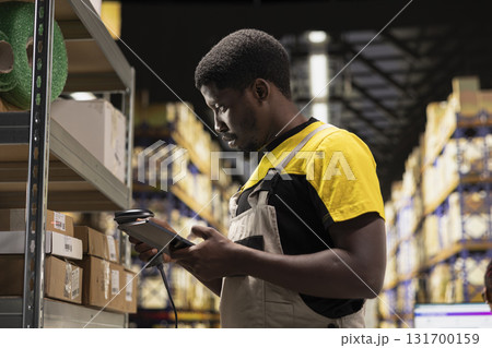 Black e-commerce employee scanning awb tracking numbers, registering shipping labels and details for the warehouse inventory records. Handling pallets import export operations. 131700159