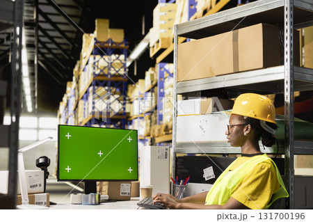 Black warehouse staff handling shipment protocols with green screen on computer, working on large business operations for retail industry. Storehouse depot filled with cardboard boxes on racks. 131700196