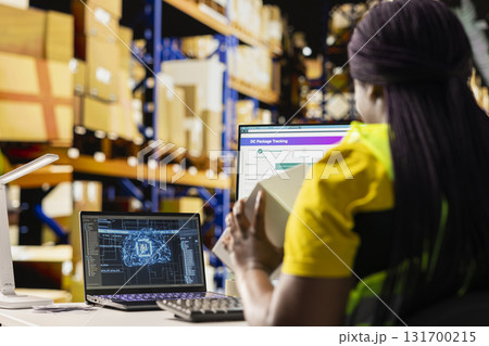 Black warehouse clerk managing orders in boxes next to AI machine learning, working on e-commerce with help from artificial intelligence neural networks. Fulfillment center tasks. Black warehouse clerk managing orders in boxes next to AI machine learning, working on e-commerce with help from artificial intelligence neural networks. Fulfillment center tasks. 131700215
