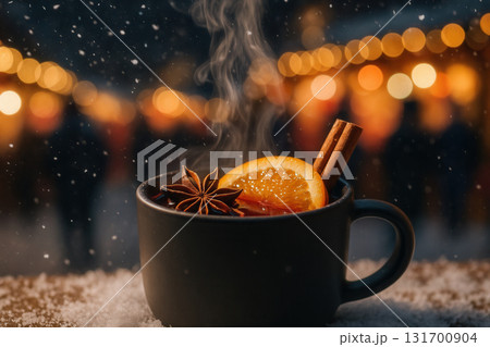 Steaming Mulled Wine In Black Mug With Orange Slice, Star Anise And Cinnamon Sticks Amid Snowfall And Festive Market Lights 131700904