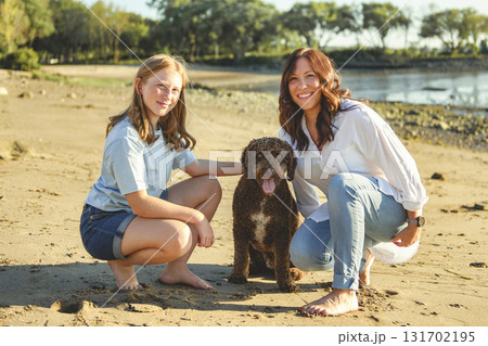 brown portuguese water dog outdoors on the beach with mother and daughter 131702195