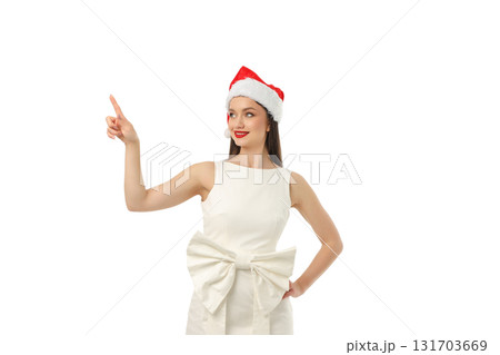 Woman in a festive Santa hat pointing with a smile, isolated, PNG 131703669