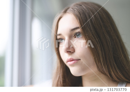 Young girl feeling anxious and unhappy looking through window Young girl feeling anxious and unhappy looking through window 131703770