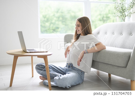 Handsome teenage girl sitting at home on the couch typing on laptop Handsome teenage girl sitting at home on the couch typing on laptop 131704703