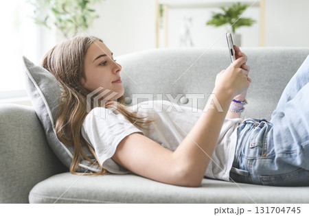Handsome teenage girl sitting at home on the couch using cellphone Handsome teenage girl sitting at home on the couch using cellphone 131704745
