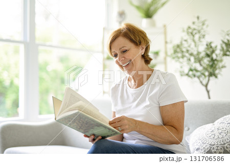 Portrait of smiling middle aged woman reading book at home 131706586