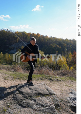 Blonde man playing string guitar outdoors in autumn forest. Concept of sound therapy, mental health and wellness rituals. Calmness tranquility audio-sensory practices. Aura farming energy 131706776