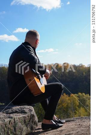 Portrait of smiling caucasian artist plays wooden acoustic guitar in autumnal park. Young songwriter plays string musical instrument hobby outside in nature fall time. Audio music healing 131706792