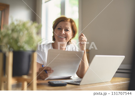 happy senior woman calculating family budget, sitting at kitchen counter with laptop, papers, happy senior woman calculating family budget, sitting at kitchen counter with laptop, papers, 131707544