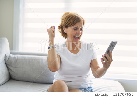 senior woman relaxing at home on the sofa reading her text messages on her mobile phone with a quiet smile senior woman relaxing at home on the sofa reading her text messages on her mobile phone with a quiet smile 131707650