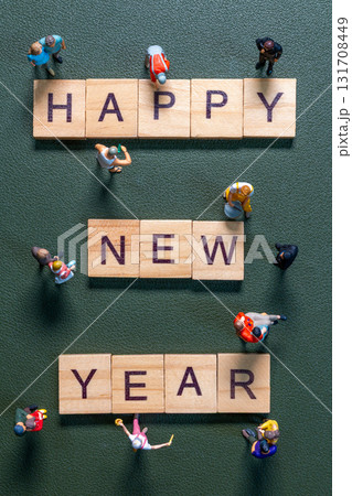 Miniature figurines surrounding wooden letter tiles forming the phrase Happy New Year 131708449
