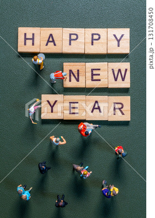 Miniature figurines surrounding wooden letter tiles forming the phrase Happy New Year 131708450