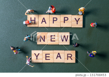 Miniature figurines surrounding wooden letter tiles forming the phrase Happy New Year 131708453