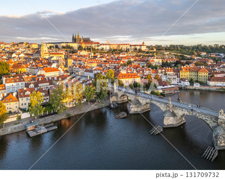 The sunrise illuminates Prague Castle and Charles Bridge over the Vltava River. The scenic old town features colorful rooftops and lush trees, creating a picturesque morning atmosphere. The sunrise illuminates Prague Castle and Charles Bridge over the Vltava River. The scenic old town features colorful rooftops and lush trees, creating a picturesque morning atmosphere. 131709732