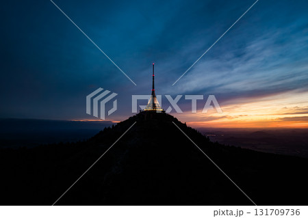 The Jested Mountain Hotel stands tall at dusk, illuminated against the evening sky. This modern structure offers stunning views over the surrounding landscape in Czechia. 131709736