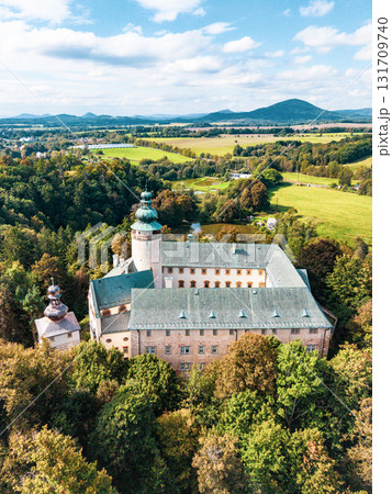 Lemberk Castle stands majestically amidst lush greenery. The aerial view highlights its historic architecture, surrounding hills, and vibrant landscape on a sunny day. 131709740