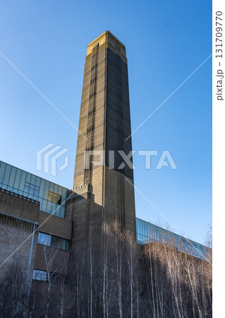 The towering chimney of Tate Modern stands against a clear blue sky in London. The unique structure reflects the gallery's modern design and its rich history as a former power station. The towering chimney of Tate Modern stands against a clear blue sky in London. The unique structure reflects the gallery's modern design and its rich history as a former power station. 131709770