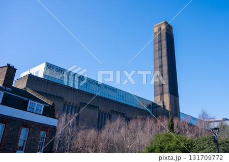 Visitors enjoy a clear day outside Tate Modern, a prominent art museum in London. The striking architecture and surrounding greenery provide a beautiful backdrop for art lovers. 131709772