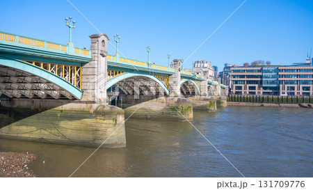 Southwalk Bridge stretches over the River Thames, showcasing its impressive structure. The clear blue sky reflects on the water, highlighting the bridge's beauty and nearby buildings. Southwalk Bridge stretches over the River Thames, showcasing its impressive structure. The clear blue sky reflects on the water, highlighting the bridge's beauty and nearby buildings. 131709776
