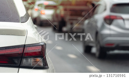 Rear side of white car driving on the road. On body of car with drop of water rain. Blurred of cars driving in line on the wet asphalt road. Rear side of white car driving on the road. On body of car with drop of water rain. Blurred of cars driving in line on the wet asphalt road. 131710591