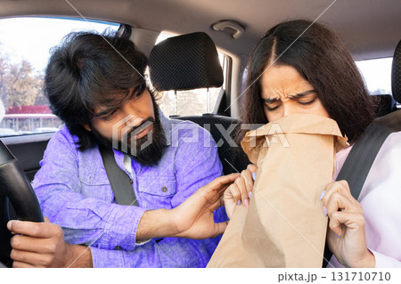 Concerned Indian man supporting his girlfriend breathing into paper bag inside car Concerned Indian man supporting his girlfriend breathing into paper bag inside car 131710710