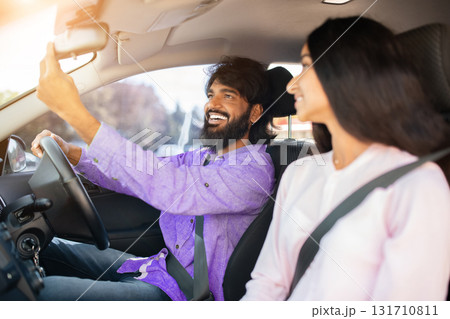 Smiling Indian man adjusting rear view mirror in car while girlfriend smiling 131710811