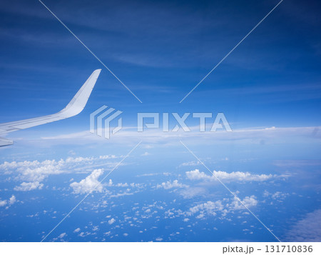 飛行機の窓から望む眼下に雲が漂う快晴の青空と飛行機の翼 131710836