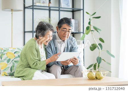 リビングでタブレット端末を見るシニアの夫婦 リビングでタブレット端末を見るシニアの夫婦 131712040