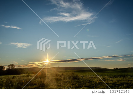 Sunset over rolling hills with vibrant colors illuminating the sky and a calm field below creating a serene atmosphere in the evening light Sunset over rolling hills with vibrant colors illuminating the sky and a calm field below creating a serene atmosphere in the evening light 131712143