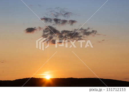Vibrant sunset over rolling hills with clouds contrasting against the evening sky at golden hour Vibrant sunset over rolling hills with clouds contrasting against the evening sky at golden hour 131712153