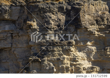 Rocky cliff formation showcasing layered textures and natural erosion in sunlight during midday hours Rocky cliff formation showcasing layered textures and natural erosion in sunlight during midday hours 131712599