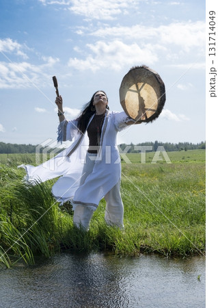 Female shaman drumming outdoors 131714049