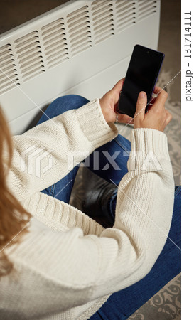Woman using smartphone near electric heater in modern cozy room Woman using smartphone near electric heater in modern cozy room 131714111