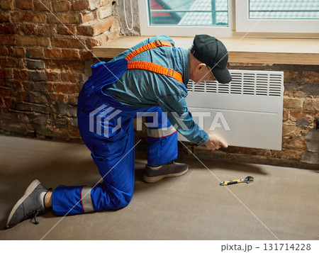 Technician installing white electric convector heater on brick wall indoors 131714228