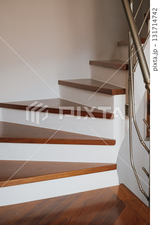 Spiral built-in staircase with brown parquet steps in interior with white walls. Spiral built-in staircase with brown parquet steps in interior with white walls. 131714742