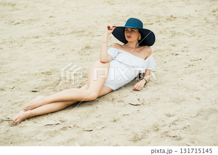 A young girl is lying on the sandy beach, emphasizing the beauty of her white swimsuit 131715145