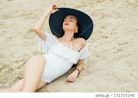 A beautiful woman in a white swimsuit is resting on the golden sand, creating a feeling of summer comfort 131715148