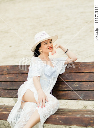 A girl in a white swimsuit and a beautiful pareo is sitting on a wooden swing A girl in a white swimsuit and a beautiful pareo is sitting on a wooden swing 131715154