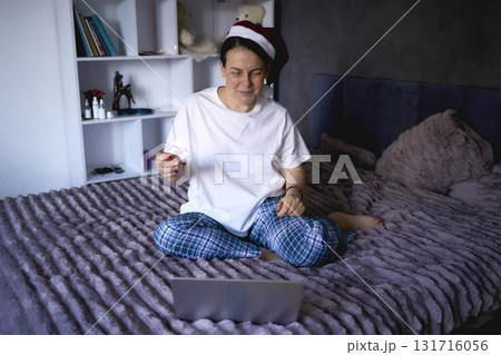 a senior woman in a Santa Claus hat and with a sparkler on a video conference wishes everyone a Merry Christmas at home via the Internet a senior woman in a Santa Claus hat and with a sparkler on a video conference wishes everyone a Merry Christmas at home via the Internet 131716056