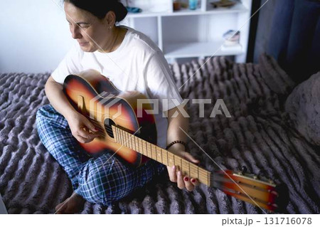 a senior woman learns to play the guitar with online lessons 131716078