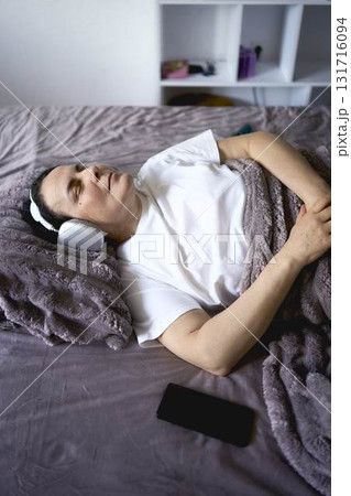 a senior woman wearing sonic hues sleep headphones sleeping under a weighted blanket a senior woman wearing sonic hues sleep headphones sleeping under a weighted blanket 131716094